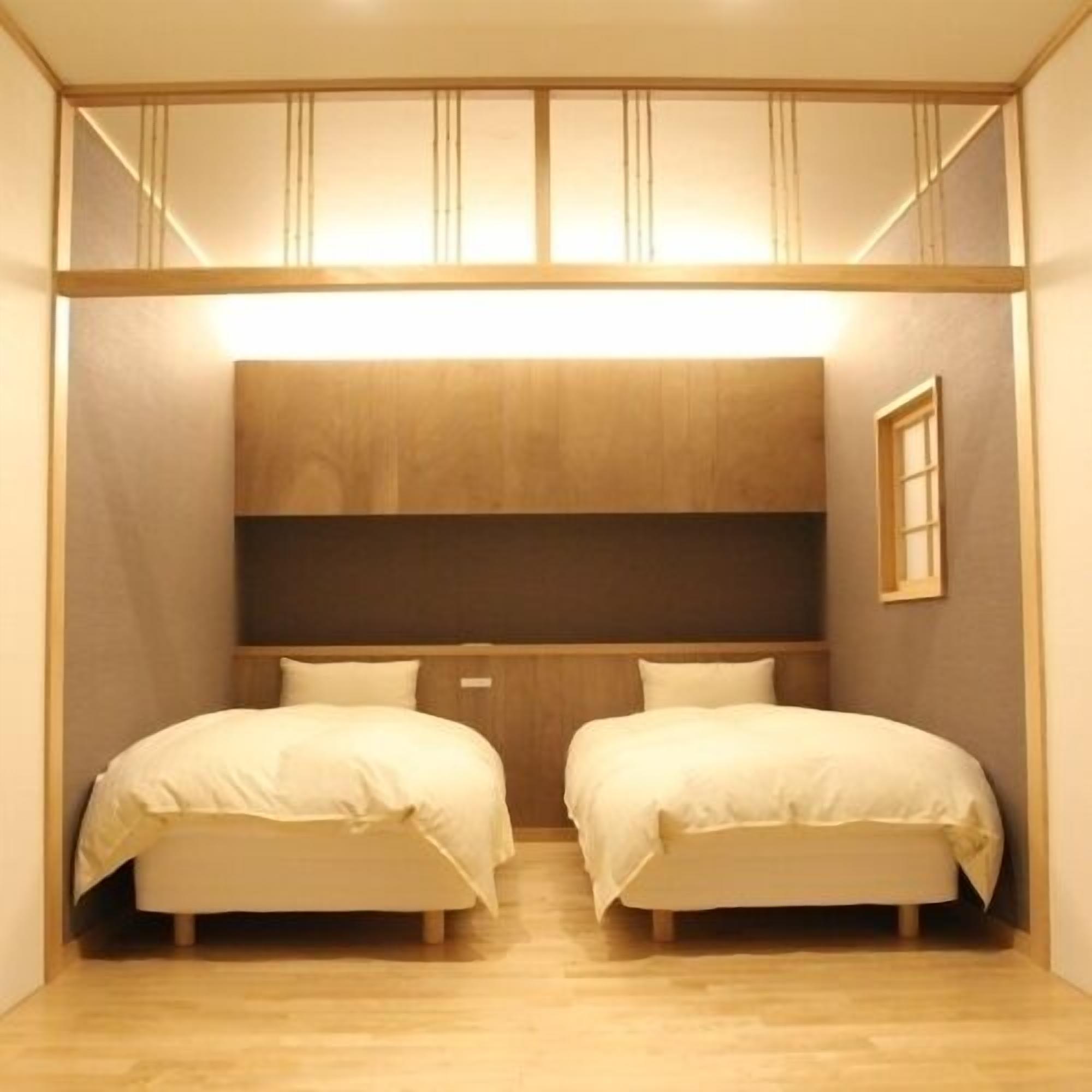 Una habitación pequeña con dos camas, cabecero de madera y una ventana discreta.