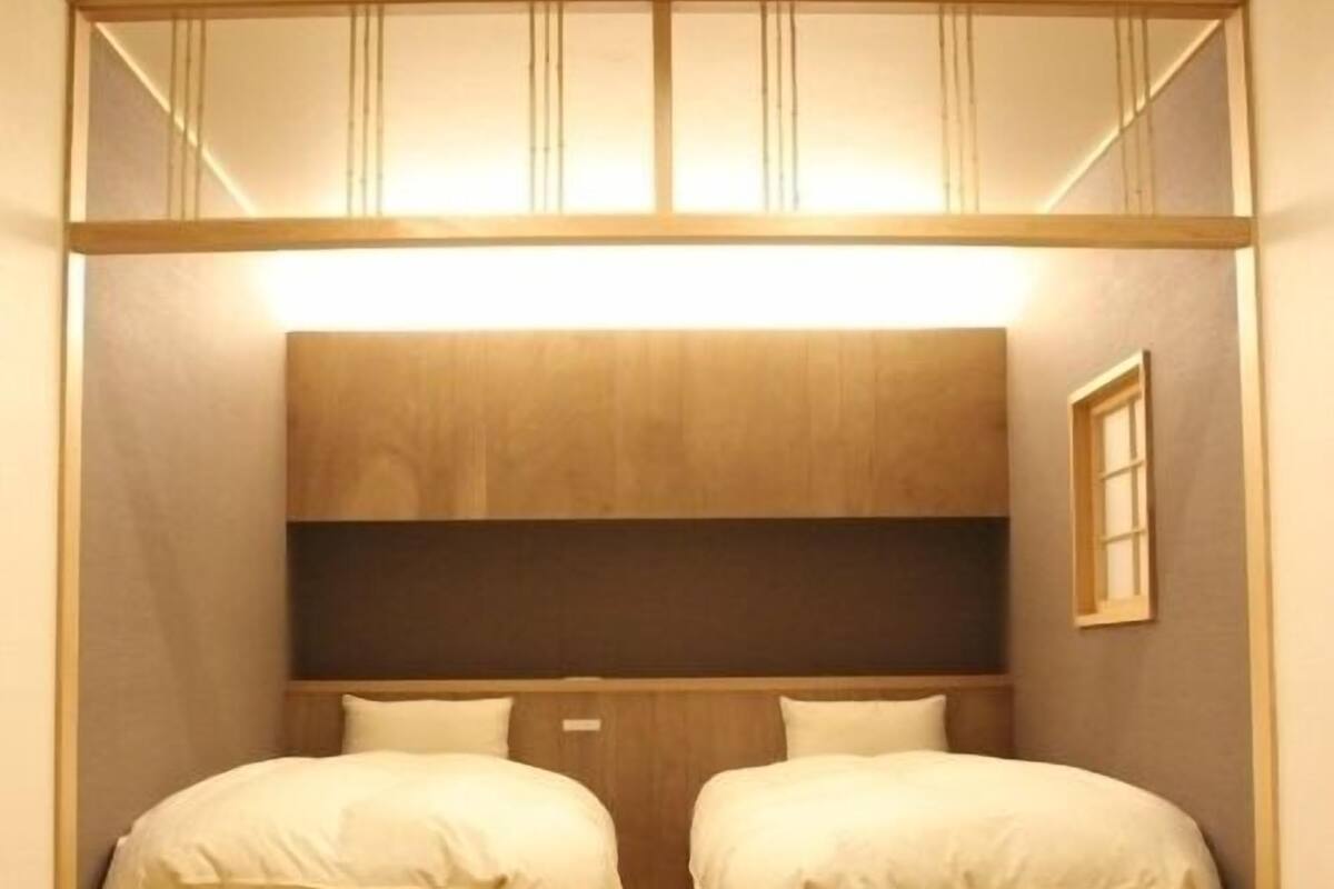 A compact room with two beds, a wooden headboard, and a small window.