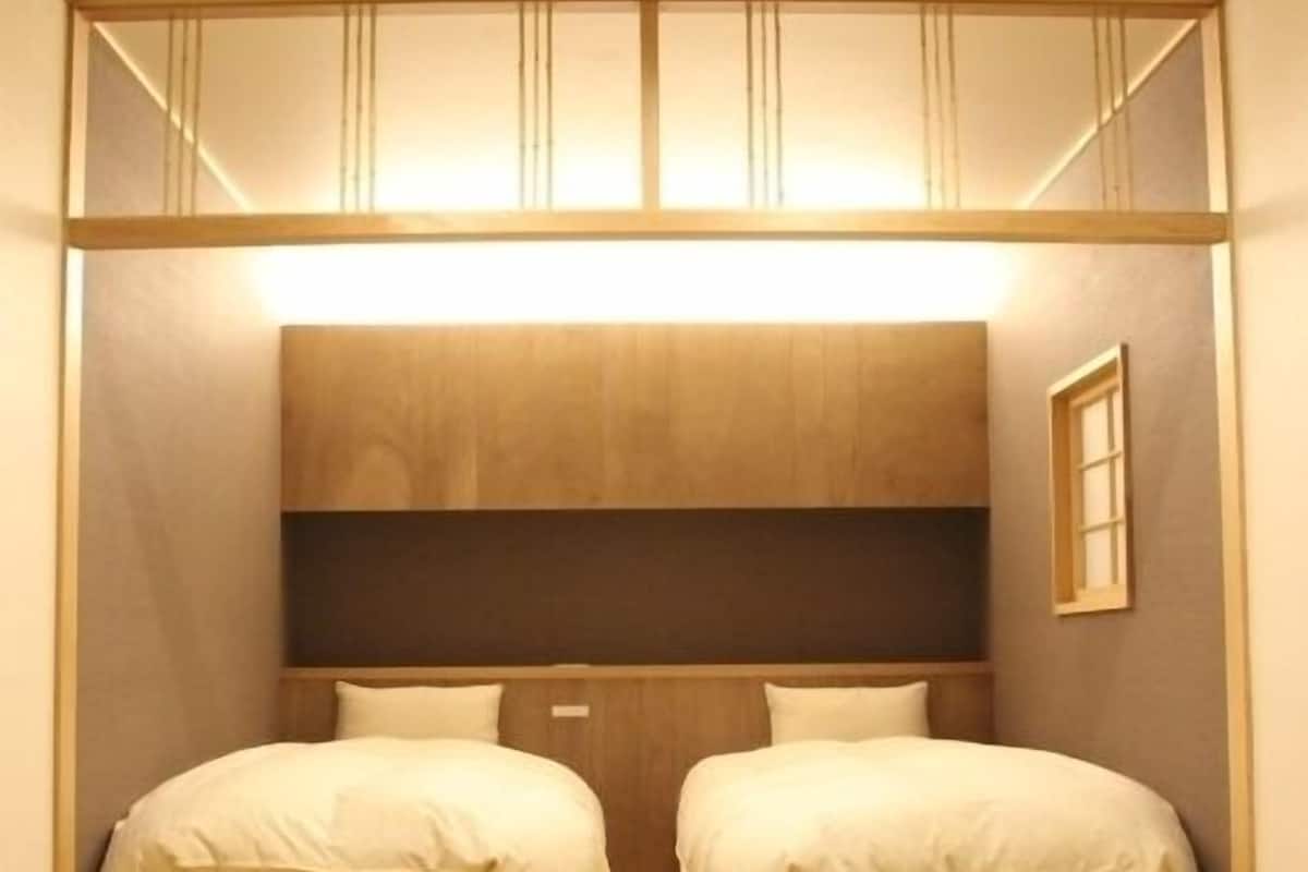 A compact room with two beds, a wooden headboard, and a small window.