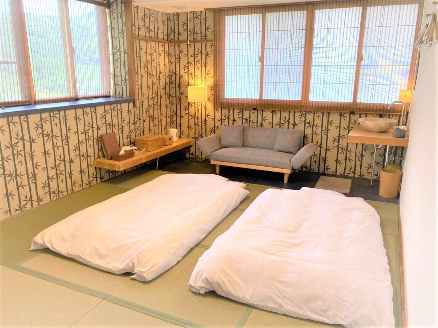 Una habitación japonesa tradicional con suelo de tatami, un futón, una mesa baja, un sofá y papel tapiz con motivos de bambú.