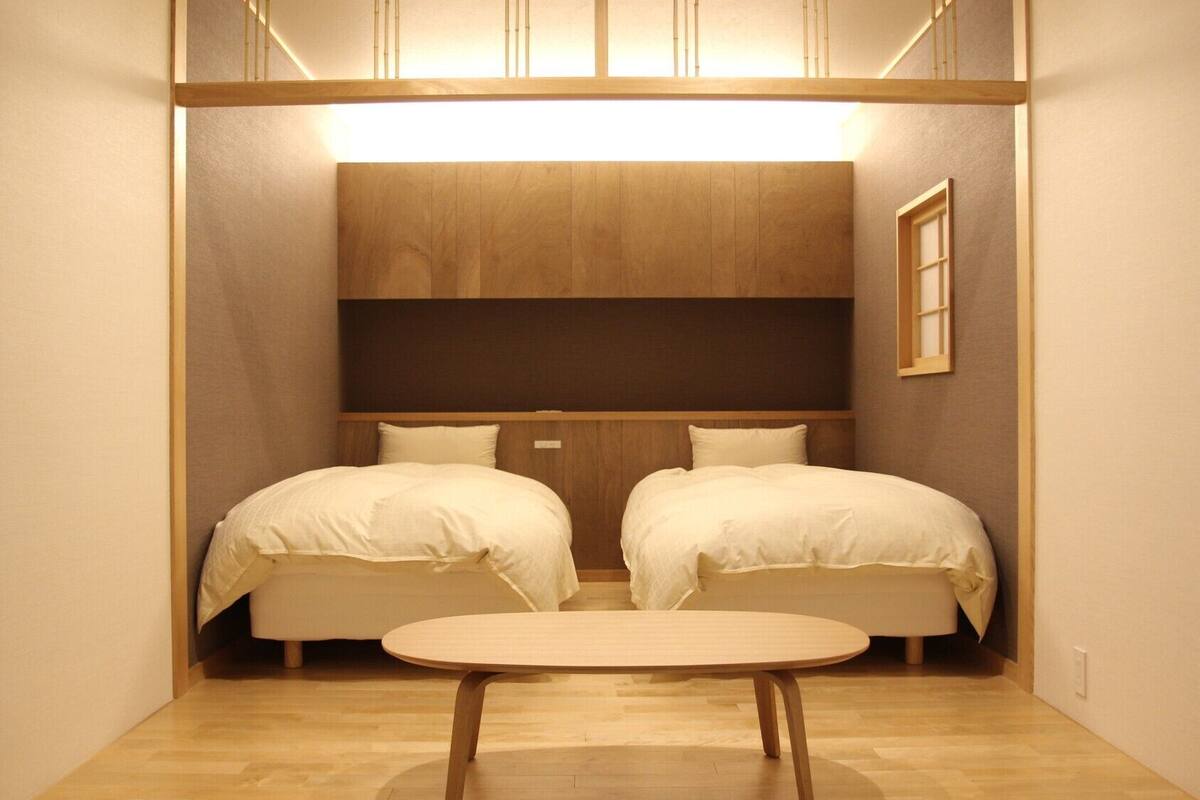 A compact room with two beds, a small table, and a wooden headboard.