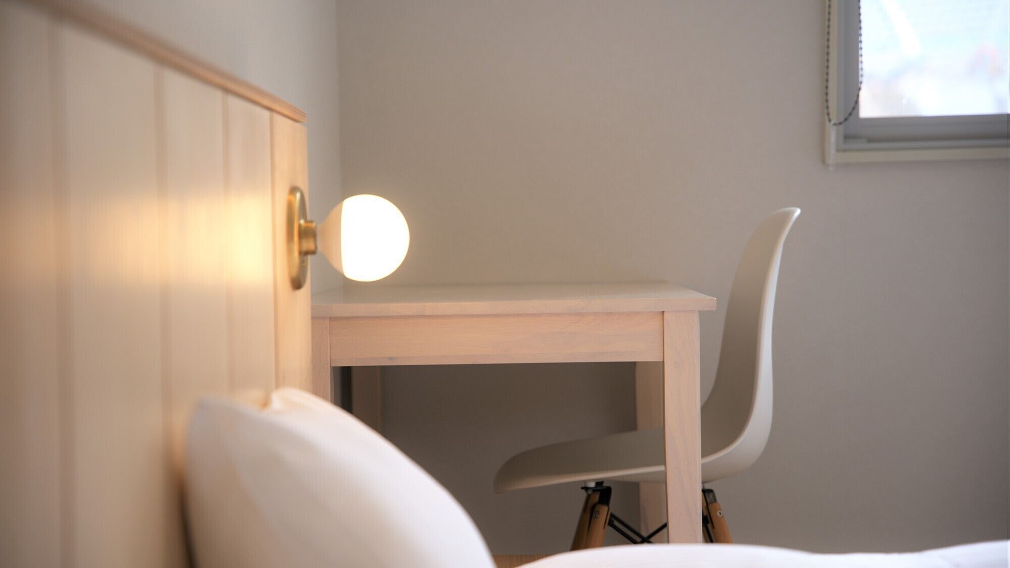 A wooden desk with a chair, a bedside lamp, and a window with blinds.