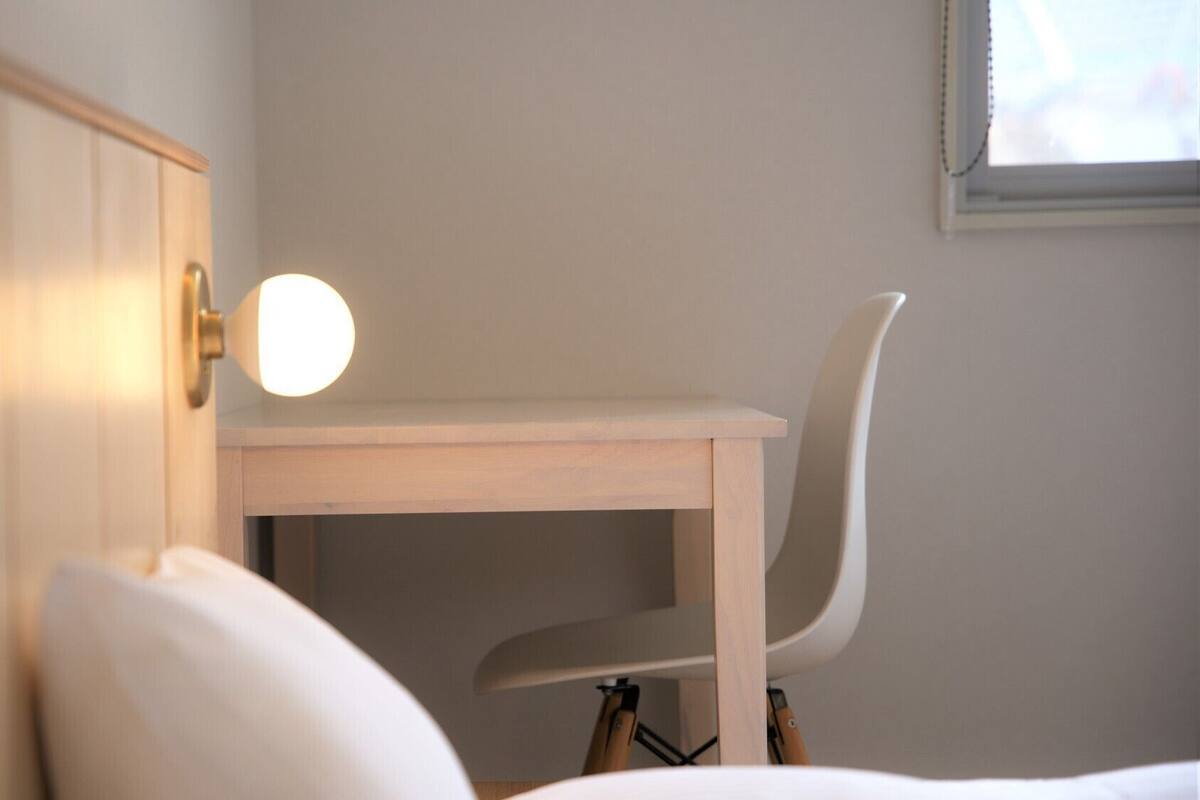 A wooden desk with a chair, a bedside lamp, and a window with blinds.