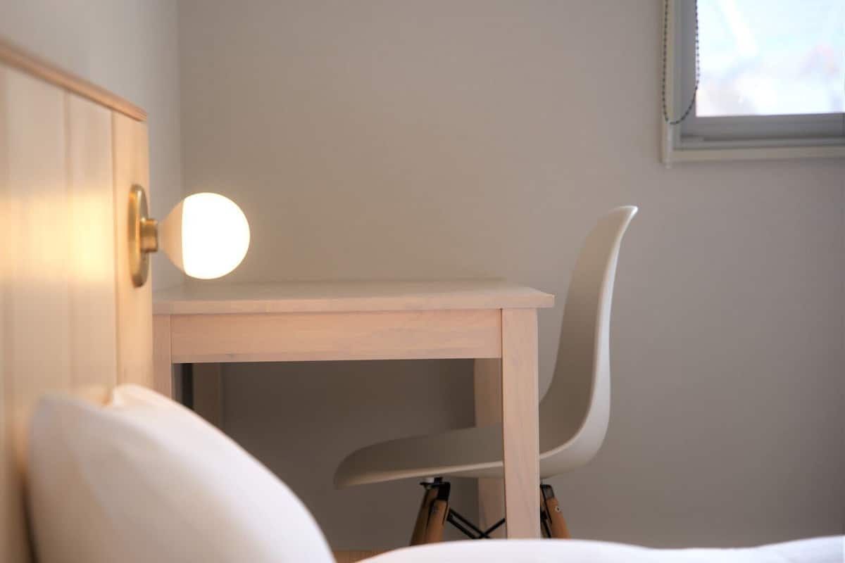 A wooden desk with a chair, a bedside lamp, and a window with blinds.