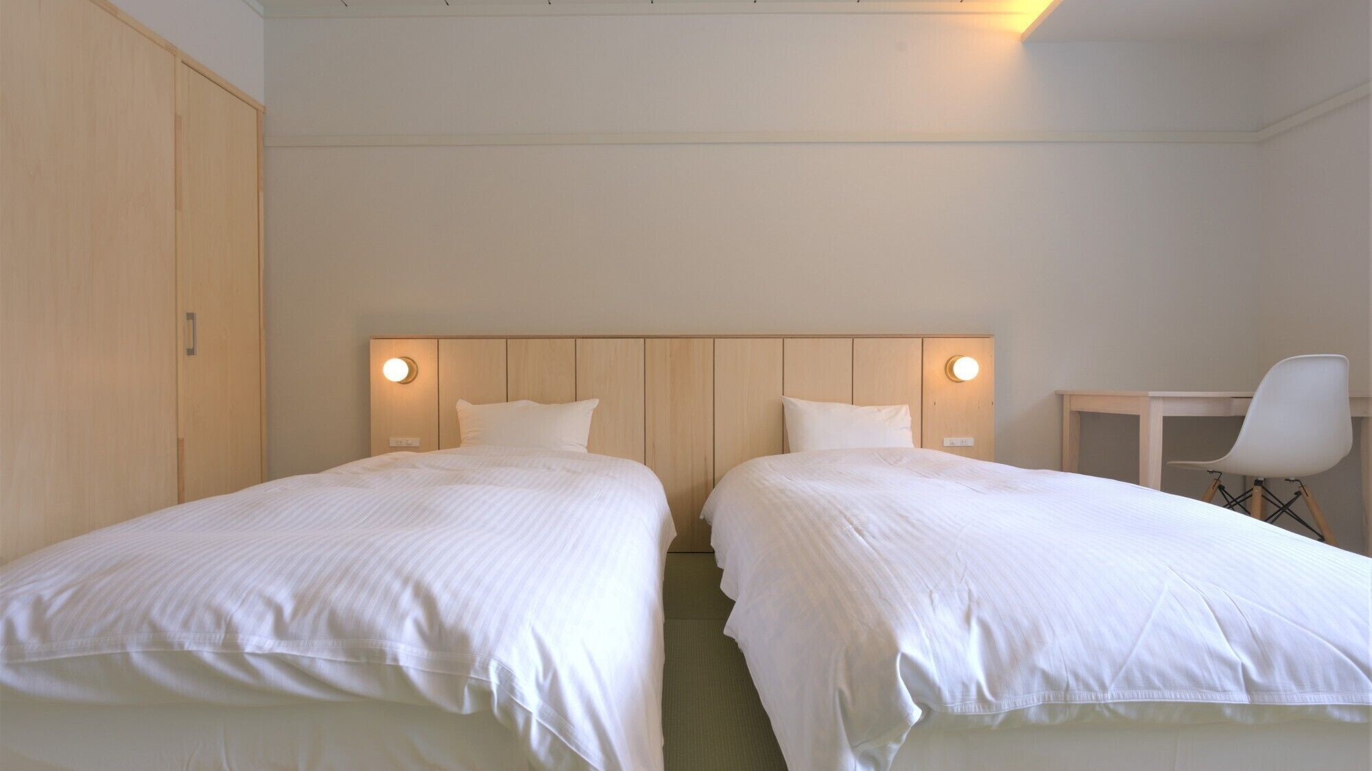 Una habitación de hotel con dos camas, un armario de madera, un escritorio y una silla.