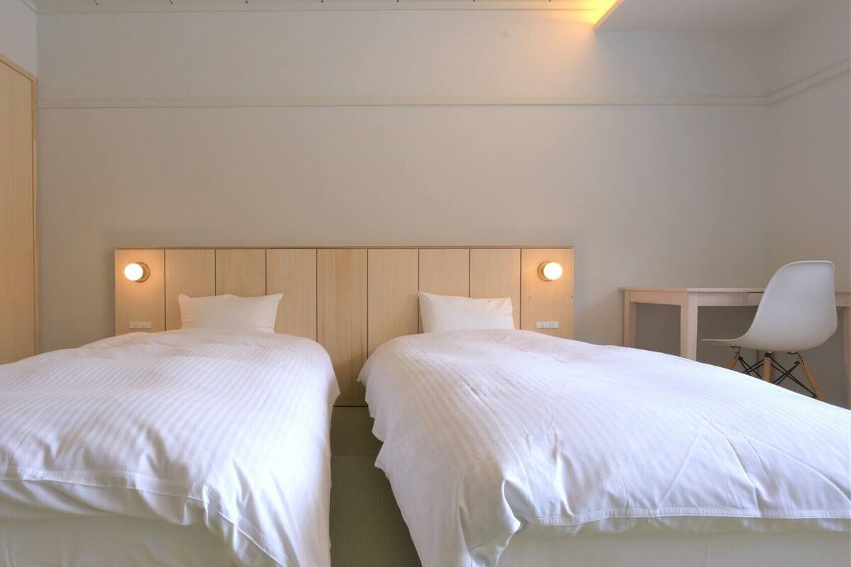 A hotel room with two beds, a wooden wardrobe, a desk, and a chair.