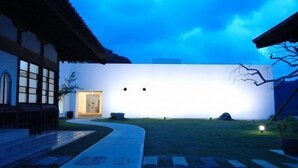 A modern building with a flat facade, a small entrance, and a pathway leading to a grassy area. - Amagi Onsen Zen no Yu (Kawazu)