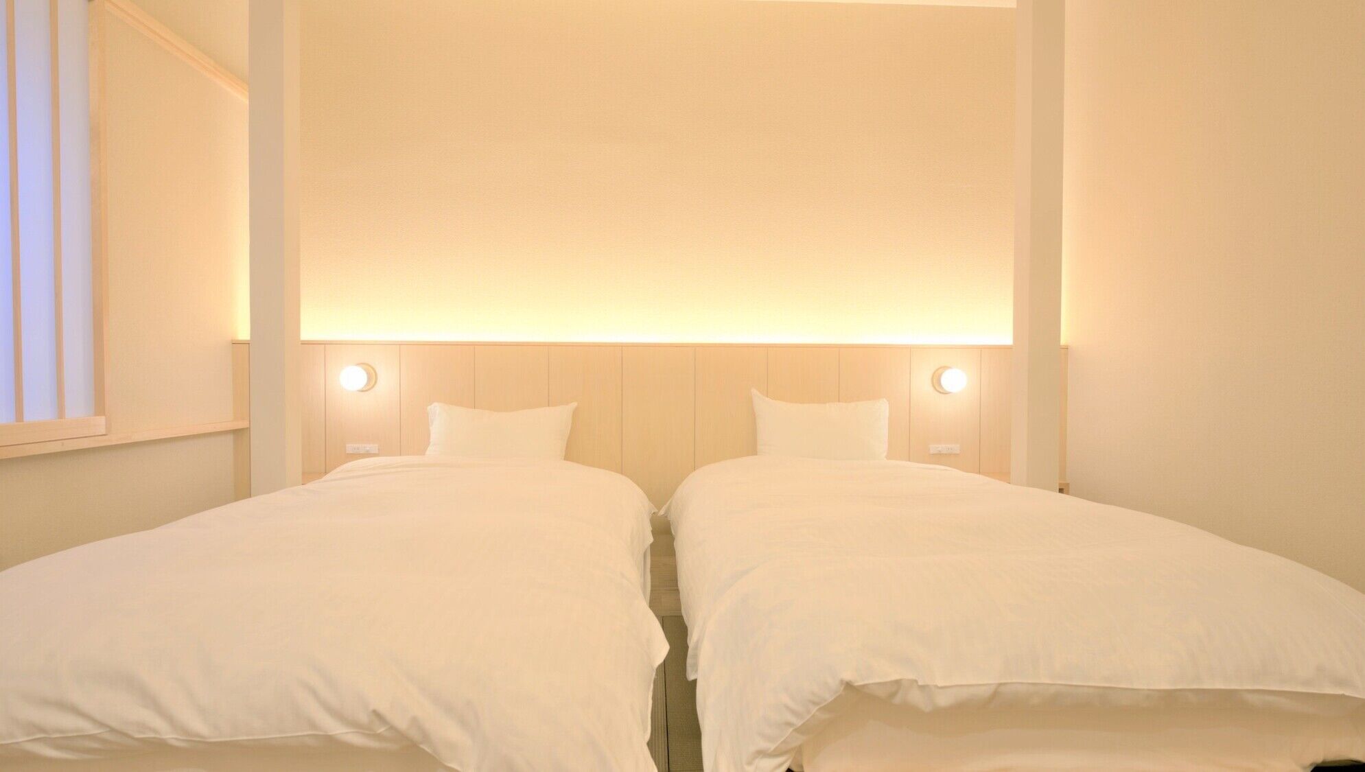A hotel room with two single beds, a wooden headboard, and wall-mounted lights.