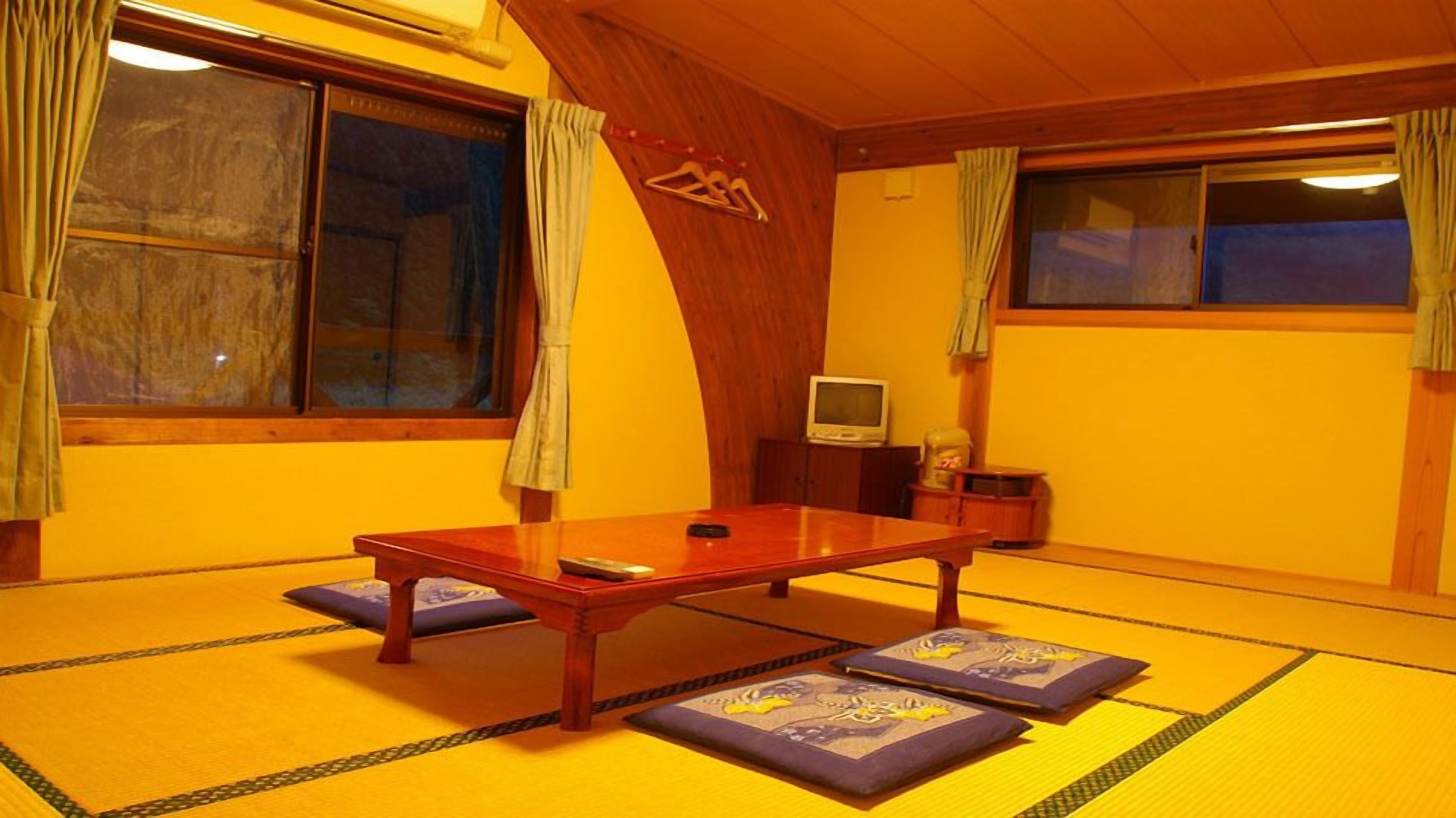 A traditional tatami mat room with a low wooden table, cushions, and a television.