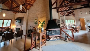 Amplia sala de estar con techo de madera, chimenea y comedor con mobiliario de madera.