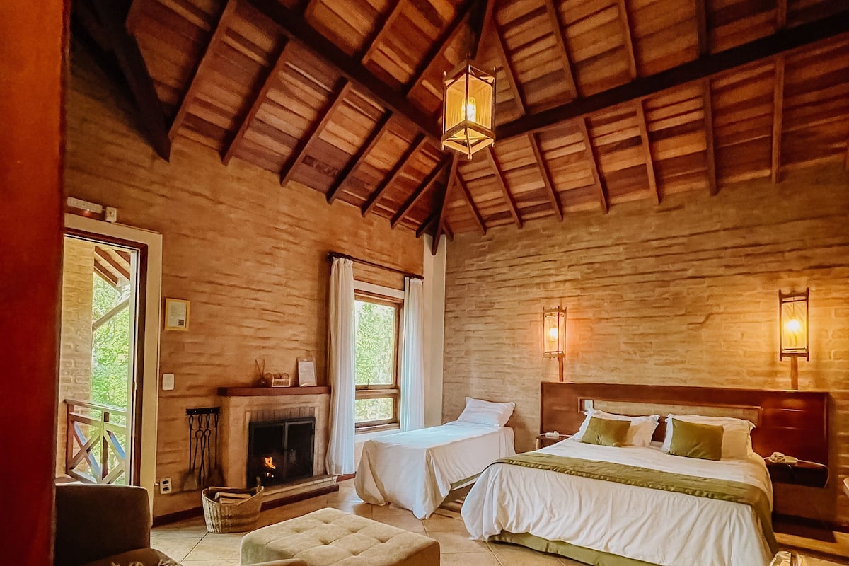 Um quarto aconchegante com lareira, duas camas, um sofá e uma janela grande.