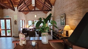 Una sala de estar acogedora con techo de madera, un sofá mullido, una mesa de centro con un oso de peluche, una planta grande y una vela.