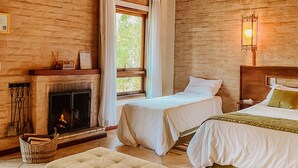 Una habitación acogedora con chimenea, dos camas, techo de madera y un amplio ventanal con cortinas.