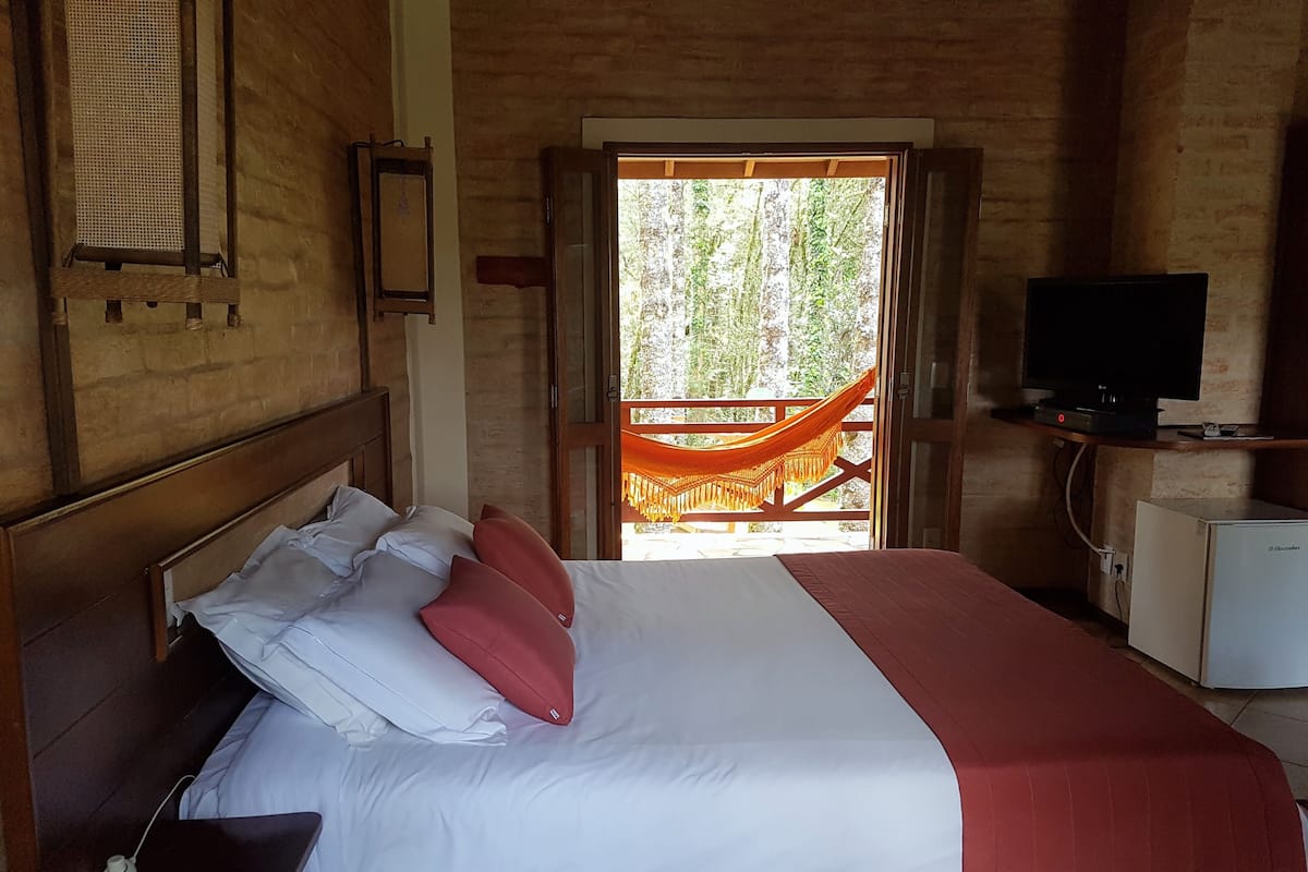 Quarto de hotel com cama, televisão e varanda com rede.