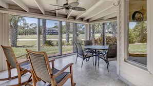A covered patio with a ceiling fan, large windows, and a table with chairs. - Belle Vue - Modern condo near beach w/ golf views (Ponte Vedra Beach)