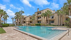 A swimming pool surrounded by palm trees and a building with balconies. - Seas the Day - Serene condo w/ pool & beach access (Ponte Vedra Beach)
