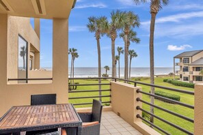 A balcony with a view of the ocean, palm trees, and a building in the background. - Seas the Day - Serene condo w/ pool & beach access (Ponte Vedra Beach)