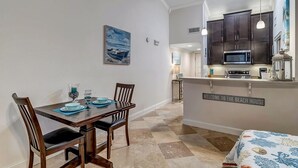 A dining area with a table set for four, a kitchen with dark cabinets and a microwave, and a sign reading "Welcome to the Beach House". - Fun in the Sun - Coastal studio w/ pool access (Ponte Vedra Beach)