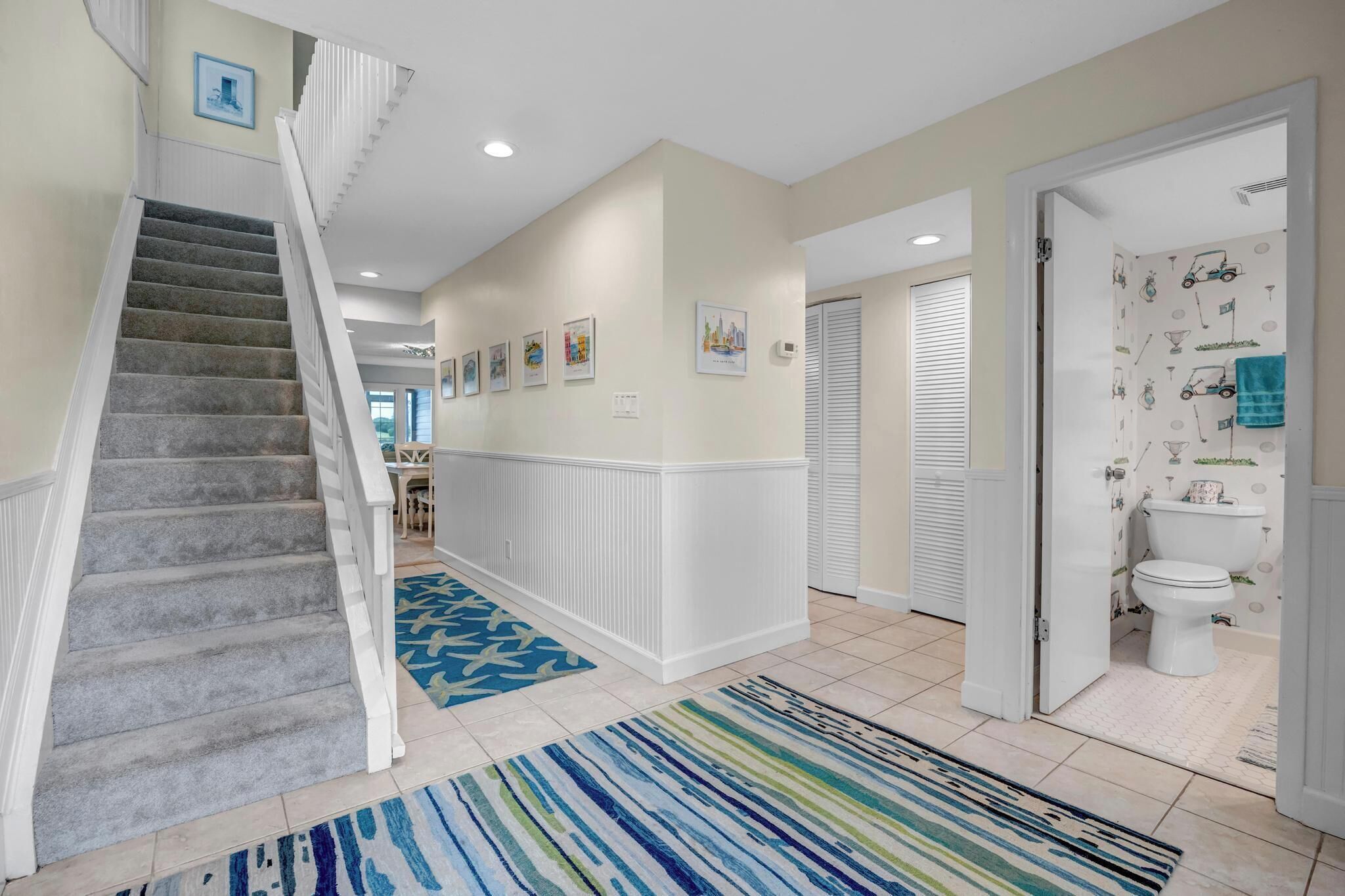 A hallway with a carpeted staircase, a patterned rug, and a bathroom with a toilet and sink.