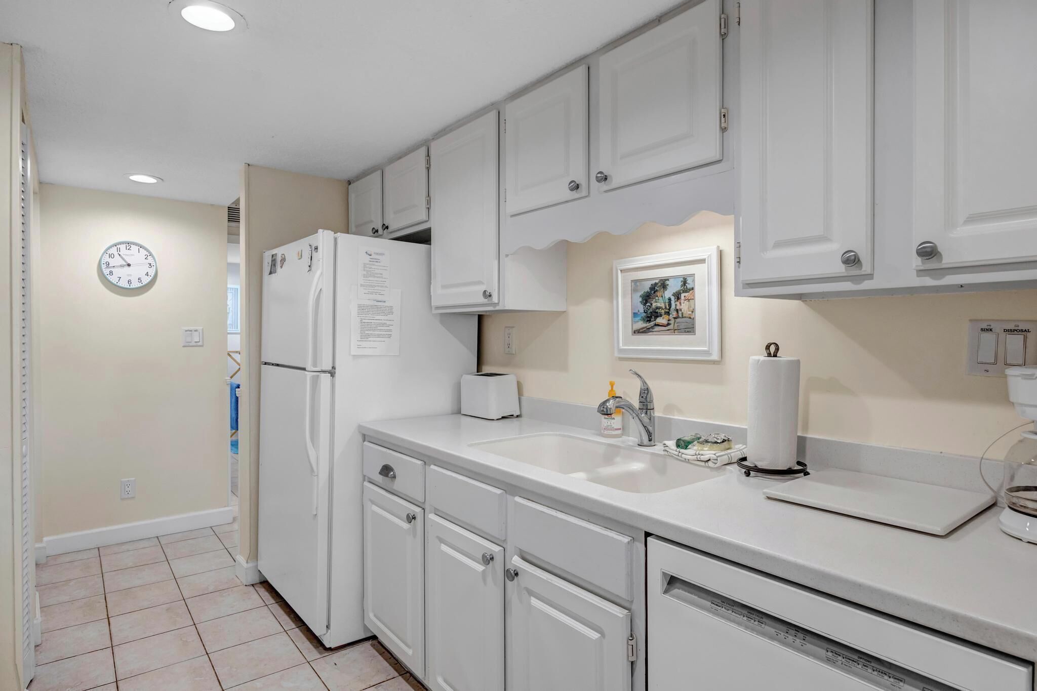 A kitchen with white cabinets, a refrigerator, a sink, and a clock on the wall.
