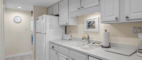 A kitchen with white cabinets, a refrigerator, a sink, and a clock on the wall.