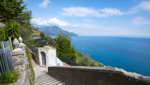 A stone staircase leading to a coastal area with a clear view of the sea and mountains in the background. - Villa Orleans (Amalfi)
