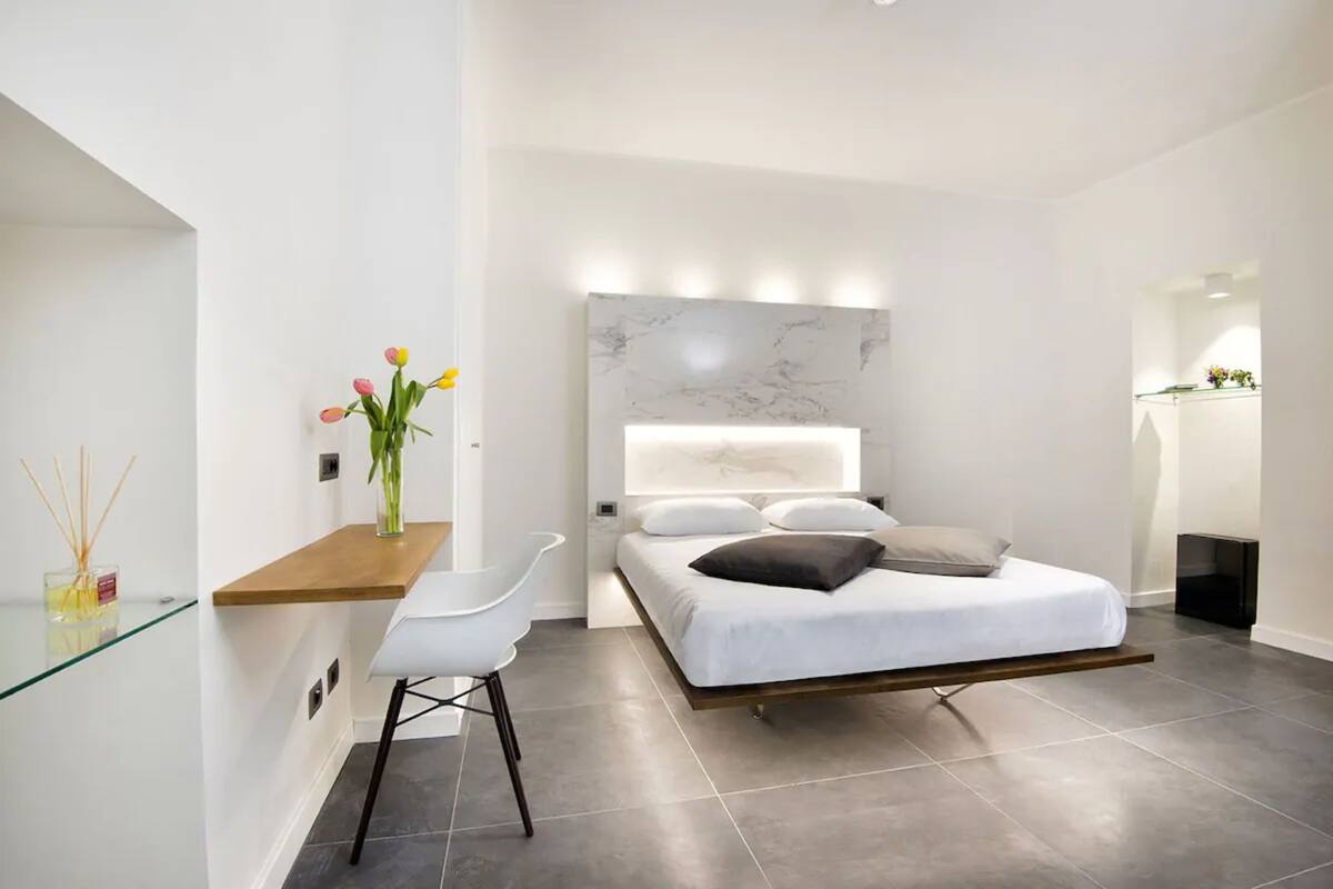 Una moderna camera da letto con un letto, un comodino, una sedia e un vaso con fiori.