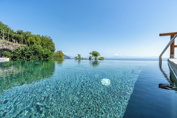 A clear pool with a wooden deck, surrounded by lush greenery and a view of distant mountains. - Villa Orleans (Amalfi)