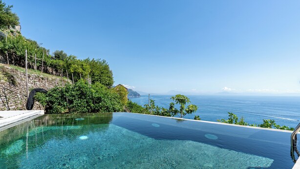 A clear infinity pool with a view of the sea and a stone wall with greenery. - Villa Orleans (Amalfi)