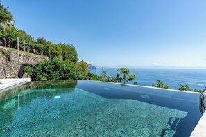 A clear infinity pool with a view of the sea and a stone wall with greenery. - Villa Orleans (Amalfi)