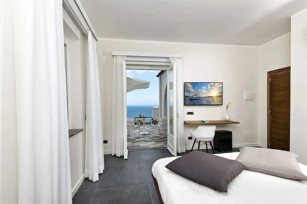 Camera d'albergo con un letto, una scrivania e un quadro raffigurante un tramonto sul mare.