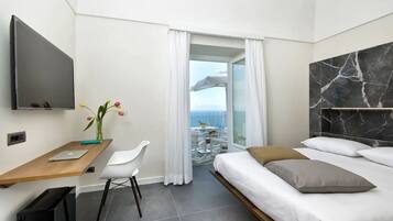 Una moderna camera d'albergo con un letto, una scrivania con un portatile, una televisione e un balcone con vista sul mare.