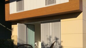 Un edificio moderno con una terraza de madera, dos sillas de mimbre y una puerta que da a un espacio interior.