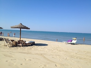 A beach with sun loungers, a thatched umbrella, and a lifeguard stand.