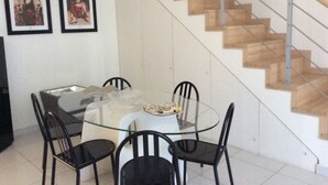 Un comedor con una mesa de vidrio y sillas, una escalera de madera y dos cuadros en la pared.