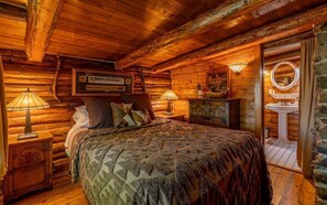 Un dormitorio tipo cabaña de troncos con cama, dos lámparas de noche, cómoda, espejo y pared de piedra.