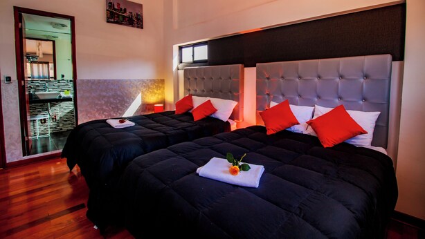 Une chambre d’hôtel avec deux lits, chacun doté d’une tête de lit capitonnée, d’oreillers rouges et blancs, et d’une petite fleur orange posée sur une serviette pliée.