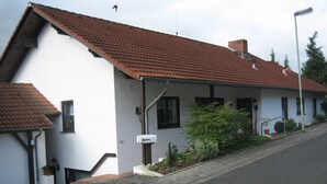 Ein zweistöckiges Haus mit rotem Ziegeldach, einer kleinen Veranda und einem Garten.