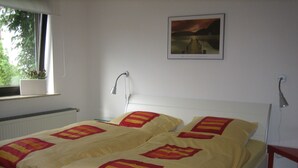 Ein ordentlich bezogenes Bett mit einer gelb-rot gestreiften Decke, einem weißen Kopfteil und einem gerahmten Bild an der Wand.
