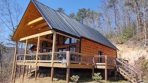 Une cabane en bois dotée d’un balcon, d’une terrasse couverte et d’un escalier menant à l’entrée principale.