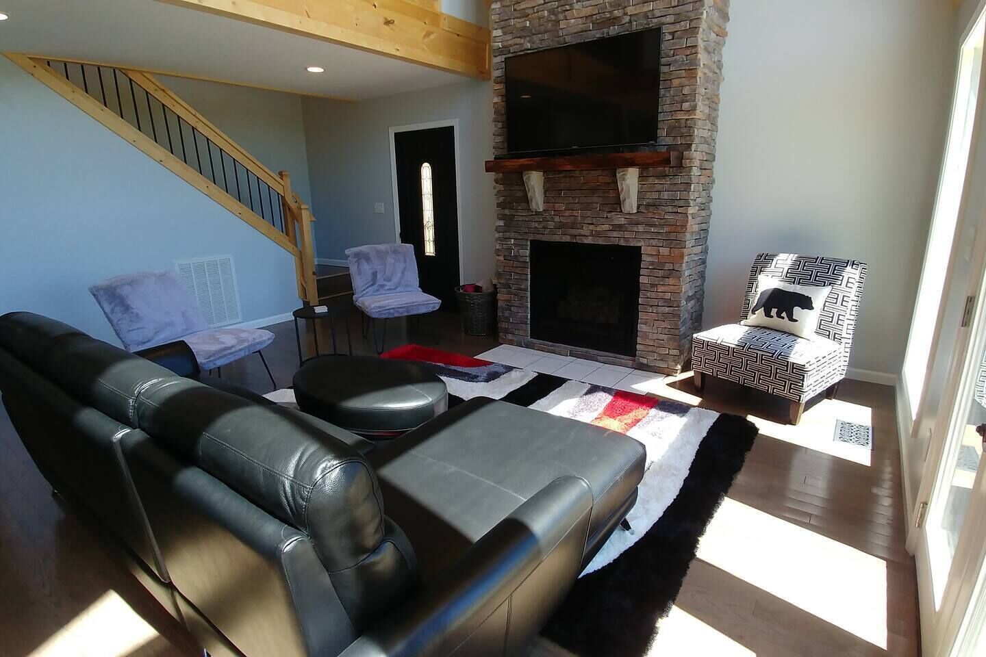 Una sala de estar con chimenea, sofá de cuero, sillón estampado y una escalera.