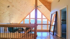Une chambre spacieuse de style loft, dotée d’une grande fenêtre, d’un plafond en bois et d’un balcon.