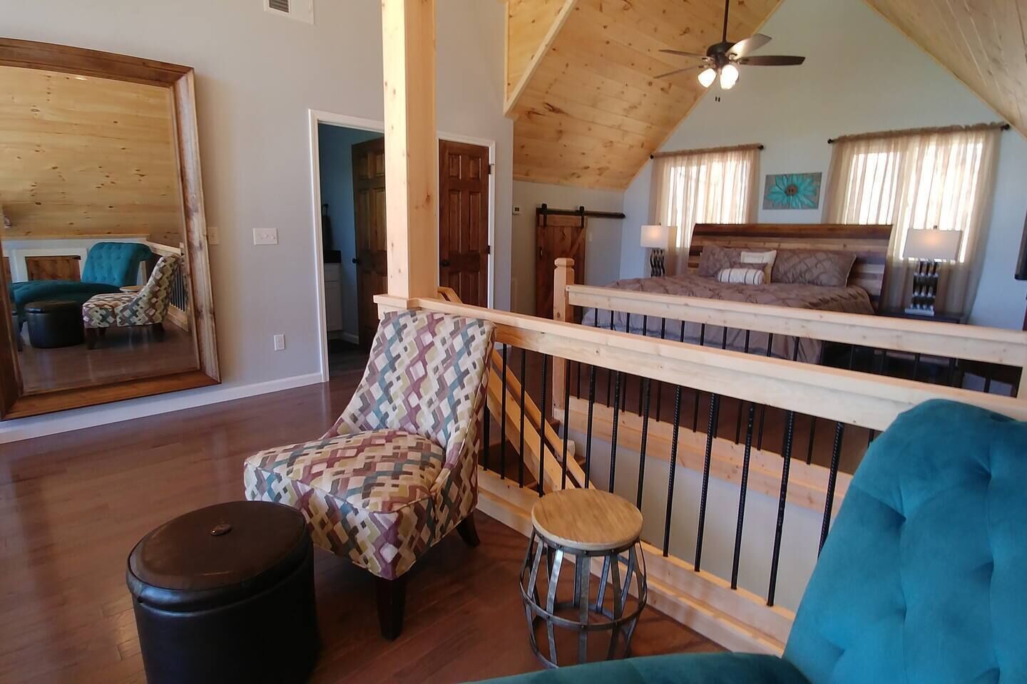 Un loft espacioso con techo alto, una escalera de madera, un espejo grande y una zona de estar acogedora con un sillón estampado y un taburete.