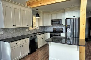 A modern kitchen with white cabinetry, a black countertop, a stainless steel refrigerator, and a built-in oven.