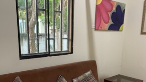 A brown sofa with plaid cushions, a glass-top coffee table, and a window with a view of trees. - Casa Campomar (Juan de Acosta)
