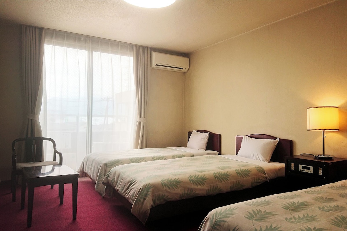 A hotel room with two beds, a chair, a desk, and a lamp.