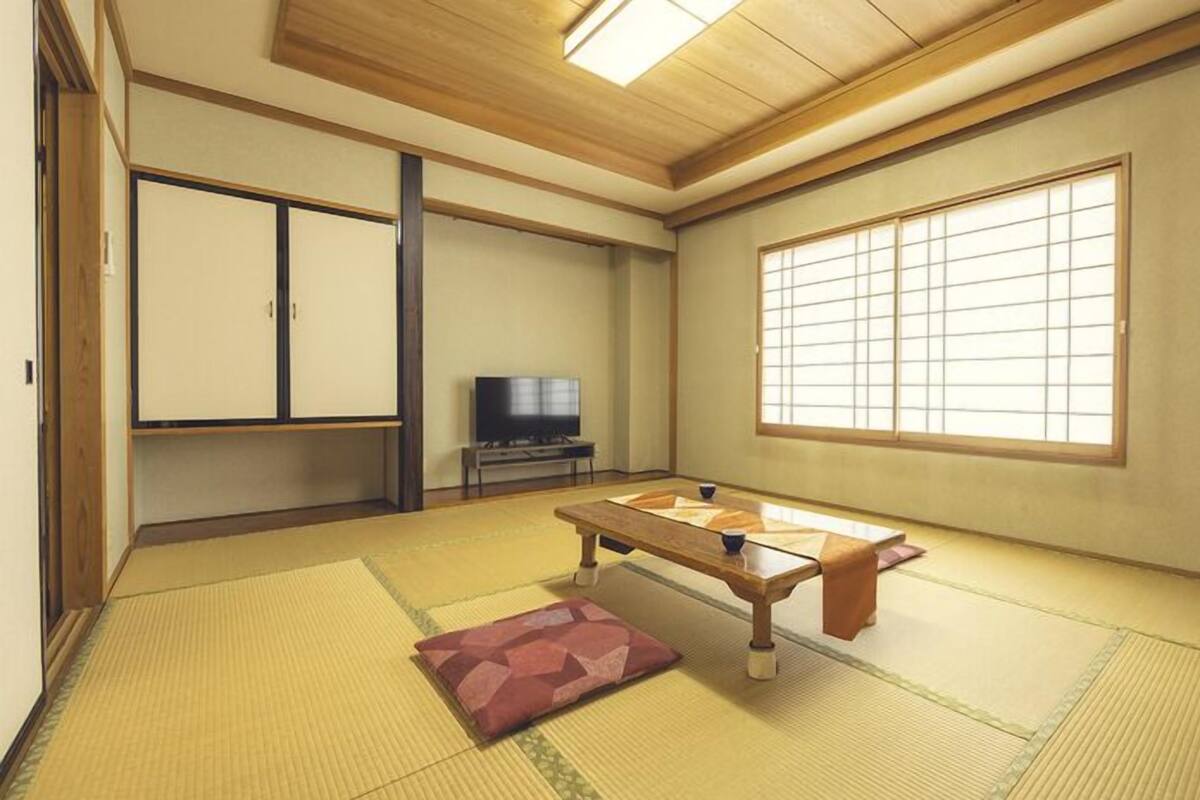 A traditional Japanese room with tatami flooring, a low table, a television, and sliding doors.