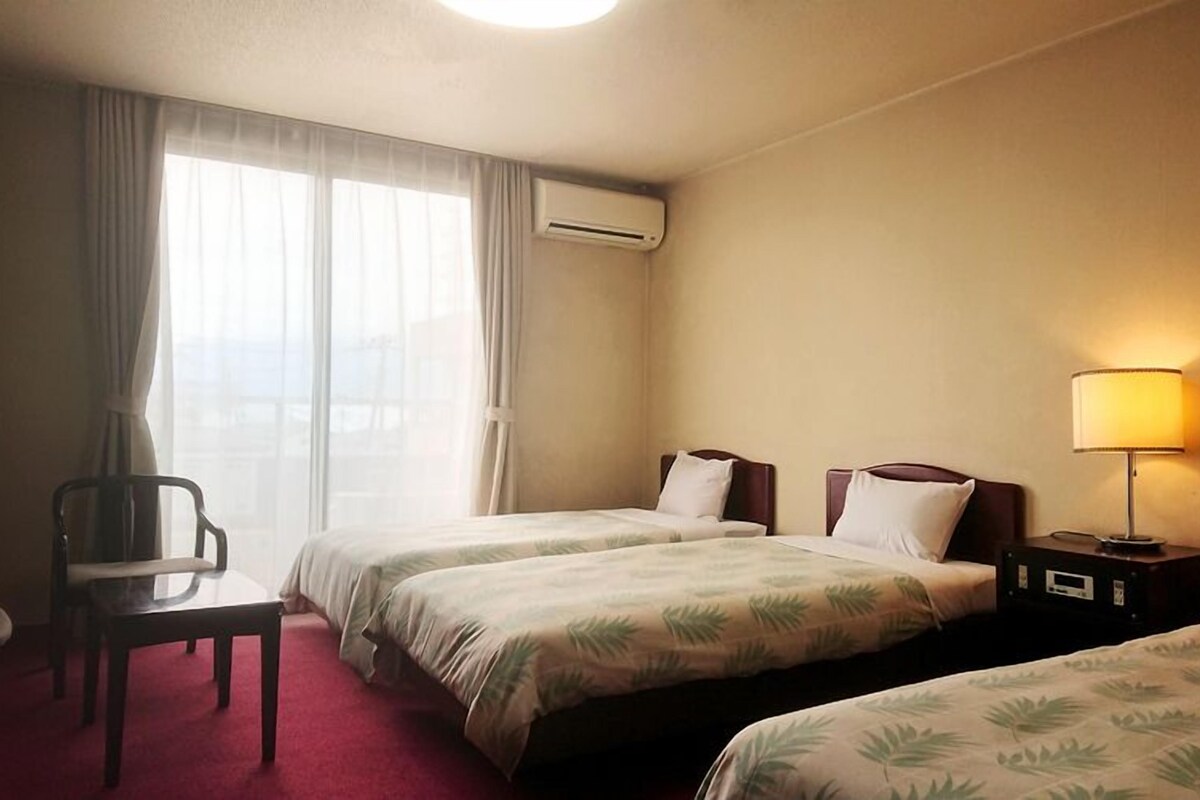 A hotel room with two beds, a desk, a chair, and a lamp.