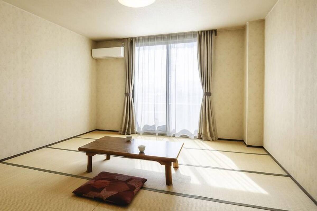 A room with tatami flooring, a wooden table, a cushion, and a window with curtains.