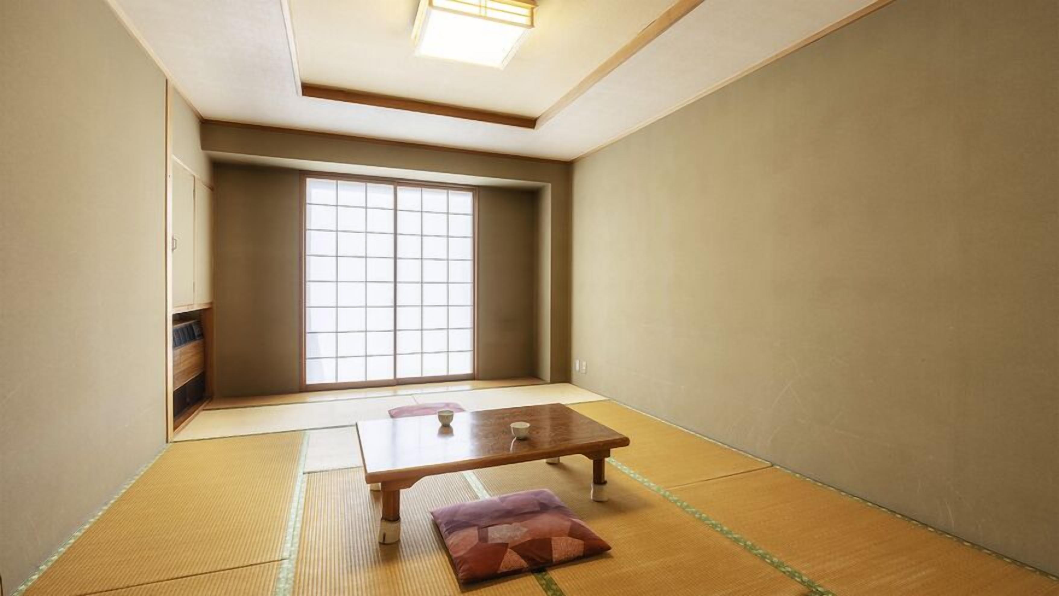 Una habitación japonesa tradicional con suelo de tatami, una puerta corredera y una pequeña mesa con cojín.